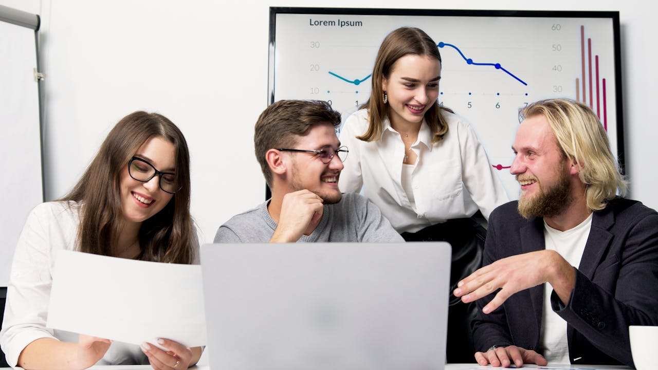 Business team engaging in a lively discussion in a modern office with charts visible in the background.